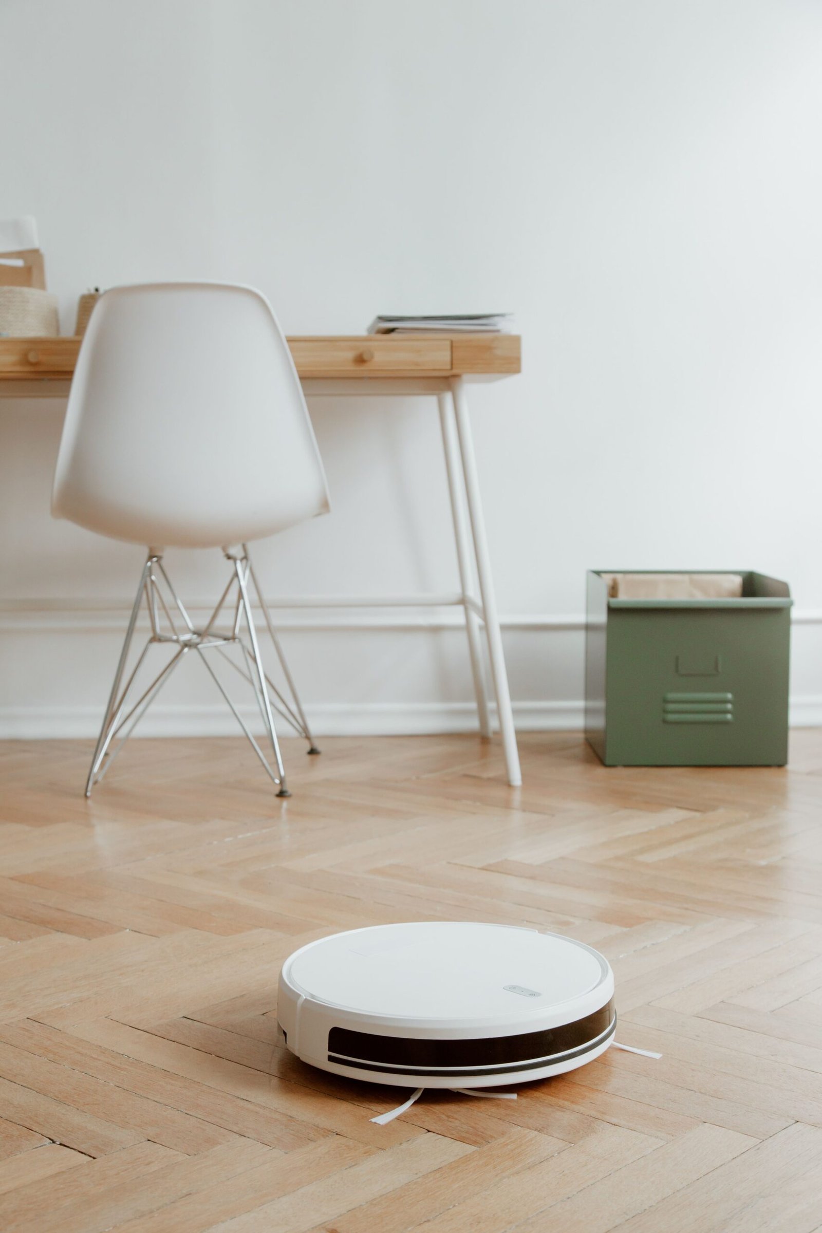 A modern minimalist room featuring a robotic vacuum cleaner on a wooden floor beside a desk and chair.